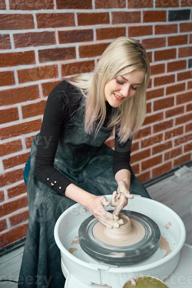 gelukkige vrouw die keramisch aardewerk op wiel maakt. concept voor vrouw in freelance, business, hobby. extra geld verdienen, hobby's omzetten in geld en passie in werk veranderen. mooie vrouw lacht foto