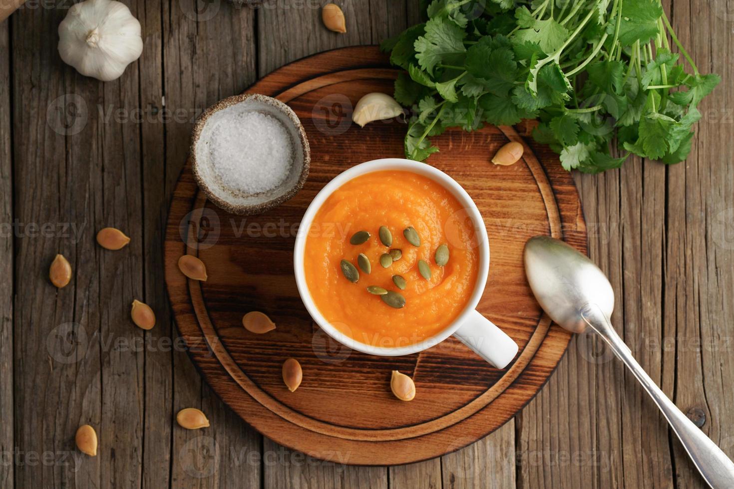 Pompoenroomsoep in beker op bruin houten tafel, bovenaanzicht. dieet vegetarische puree op snijplank met peterselie, knoflook. foto