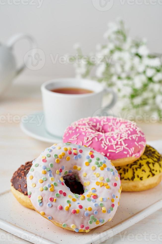 donuts en thee. helder, kleurrijk junkfood. verticaal. licht beige houten achtergrond foto