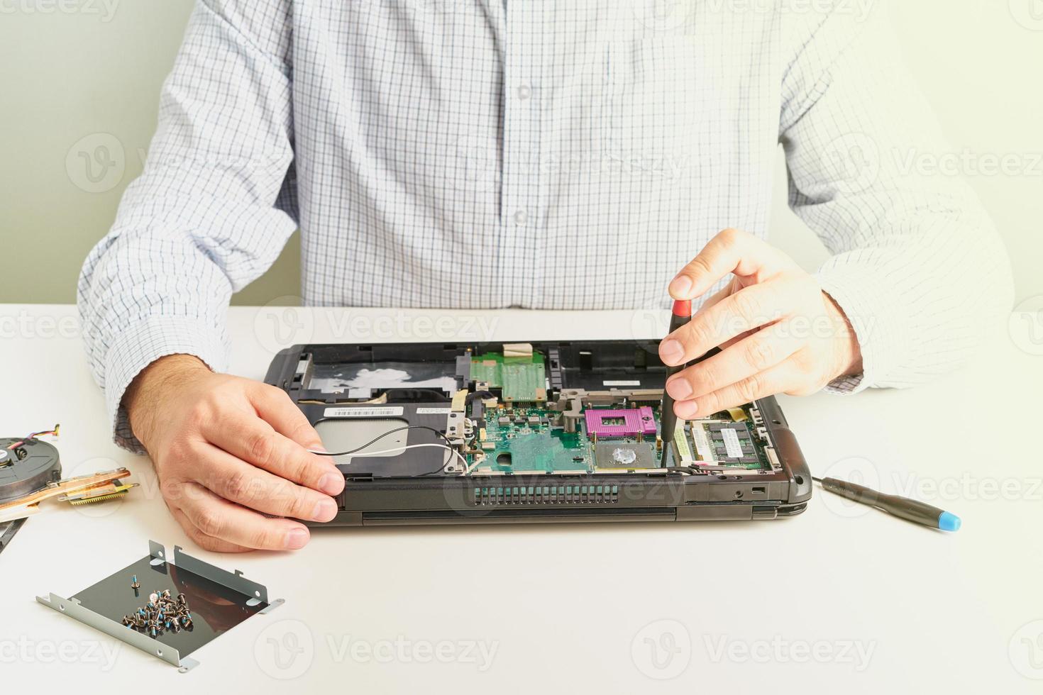 man repareert computer. een servicemonteur in shirt repareert laptop, aan een wit bureau tegen een witte muur. foto