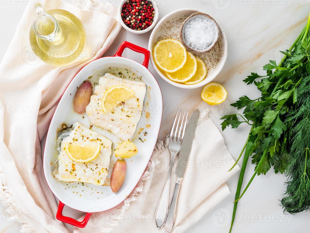 kabeljauwfilet, vers gekookt in oven met ui in porseleinen schaal om te bakken, citroen op bord foto