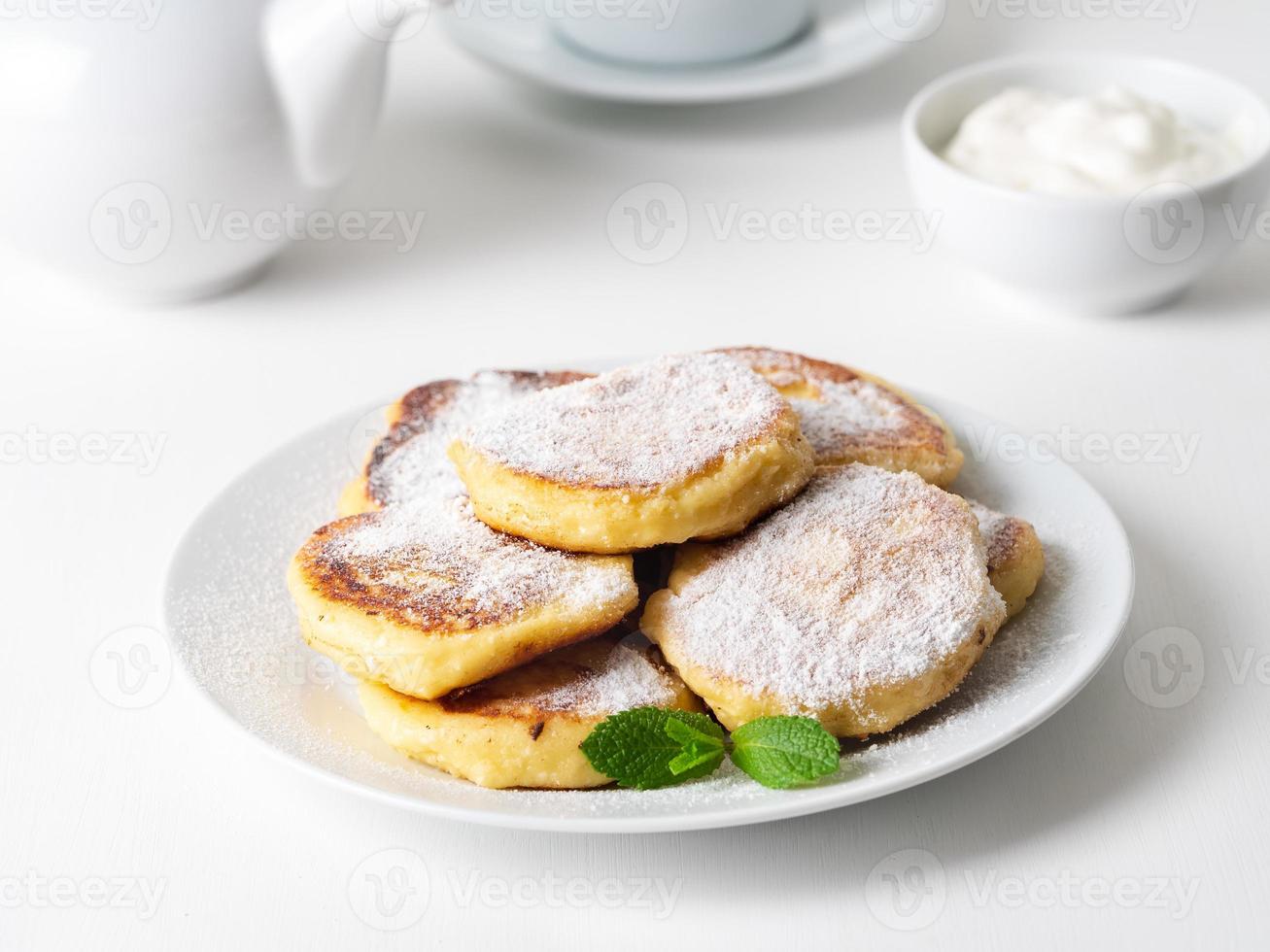 cheesecake, wrongelbeignets. kwarkpannenkoekjes met poedersuiker. zoete gebakken kaas pannenkoeken op witte plaat op witte achtergrond. theekransje thuis foto