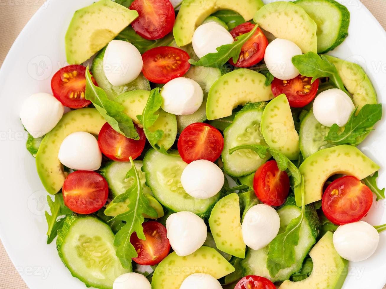 frisse salade - tomaten, komkommers, rucola, mozzarella, avocado. olie met kruiden, rozemarijn tijm, bovenaanzicht, close-up foto