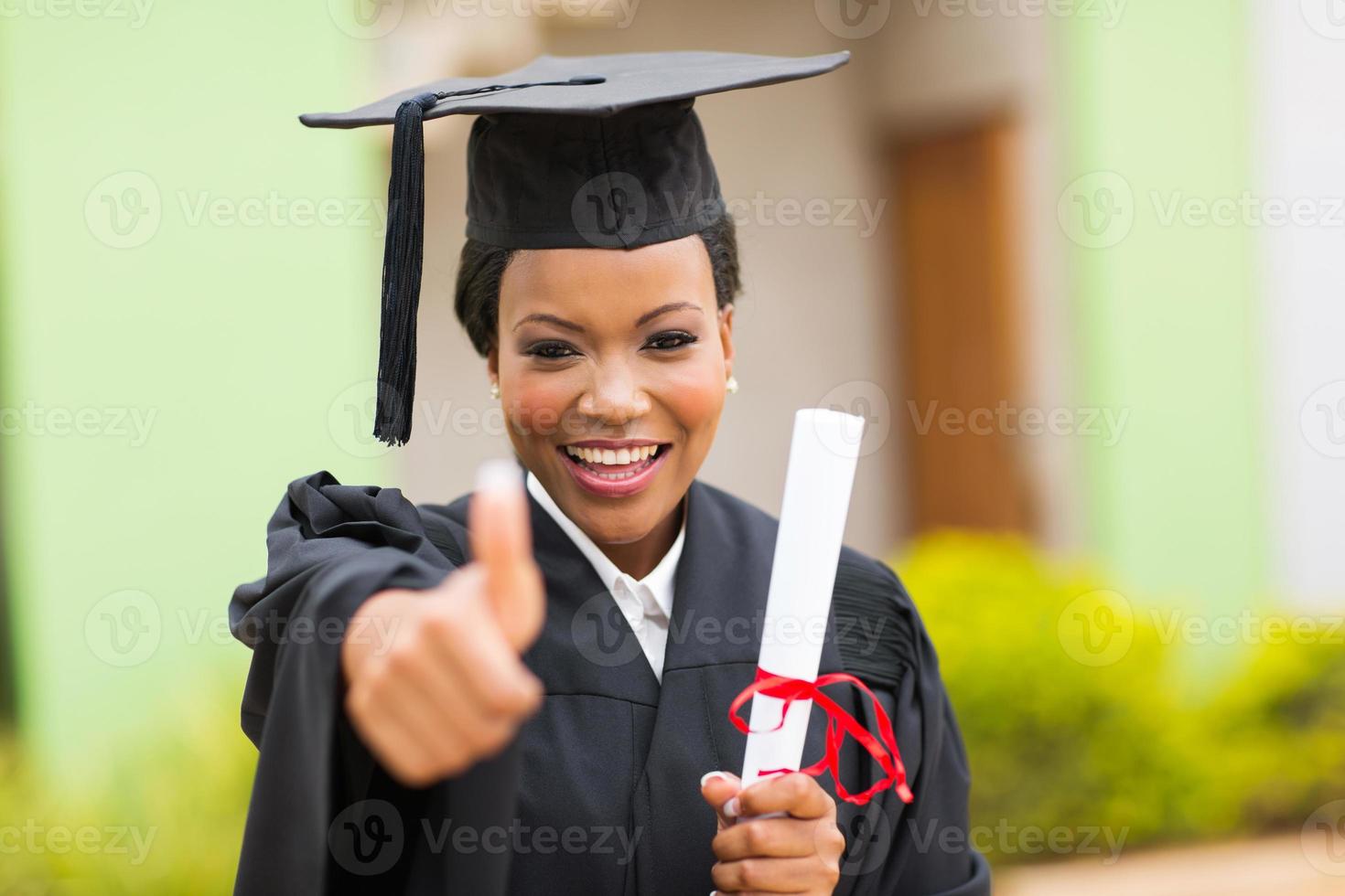 Afrikaanse vrouwelijke afgestudeerde duim opgevend foto