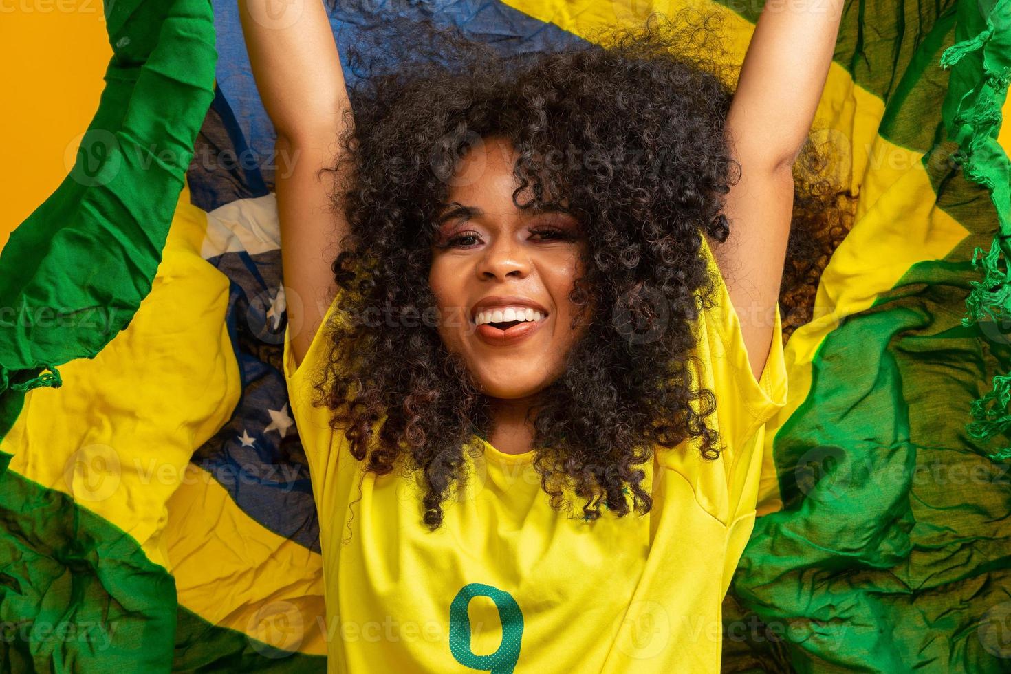 afro meisje juichen voor favoriete braziliaanse team, met nationale vlag op gele achtergrond. foto