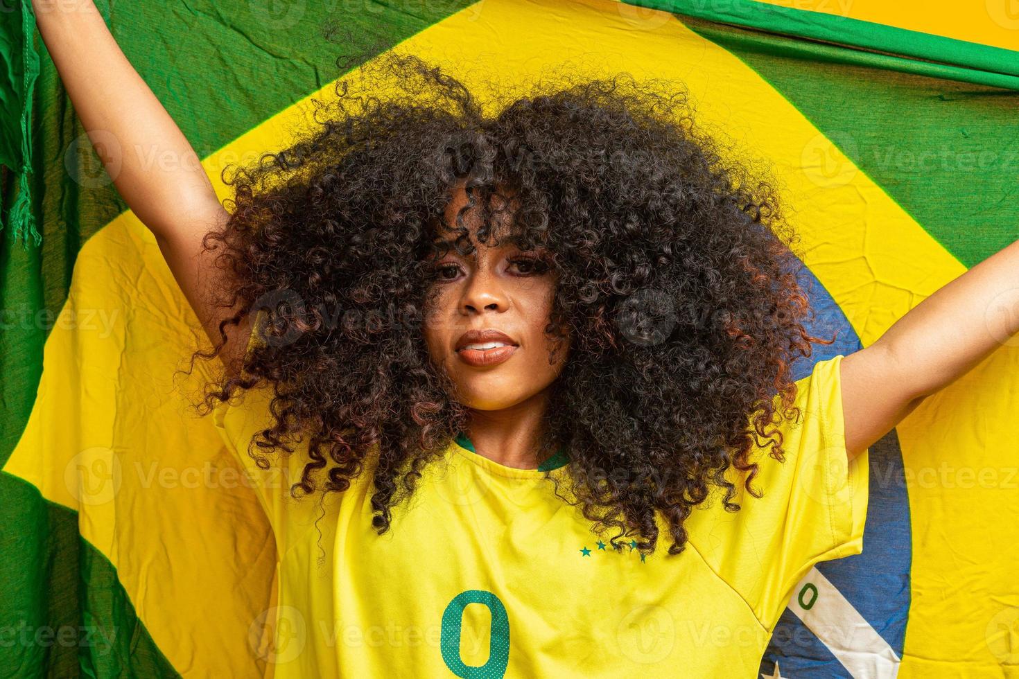 afro meisje juichen voor favoriete braziliaanse team, met nationale vlag op gele achtergrond. foto