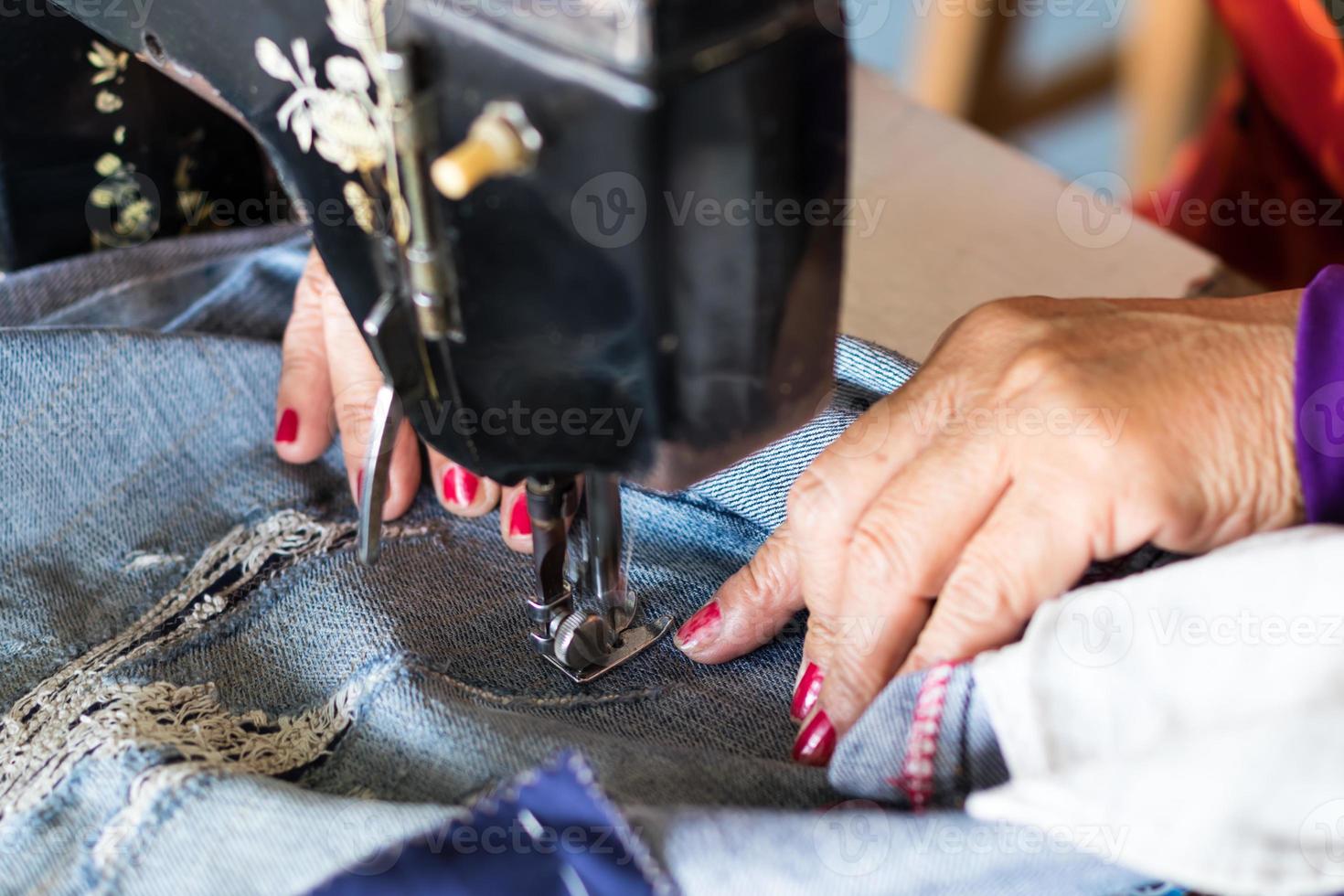 rode nagel hand naaien jeans reparatie. foto