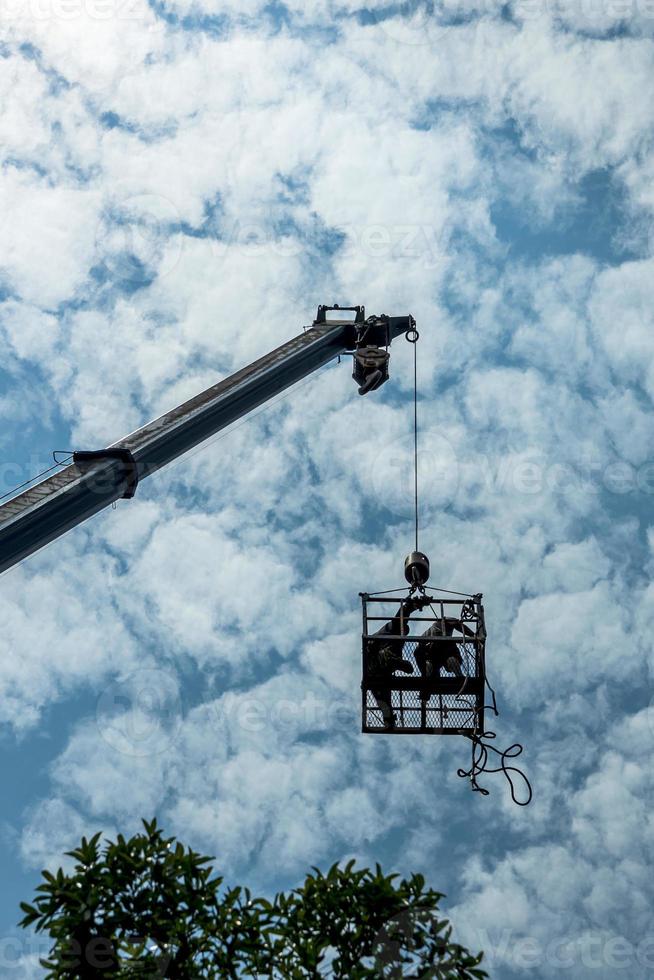 lage hoekmening, een arbeider in een stalen mand stijgt overdag boven de boomtop uit. foto