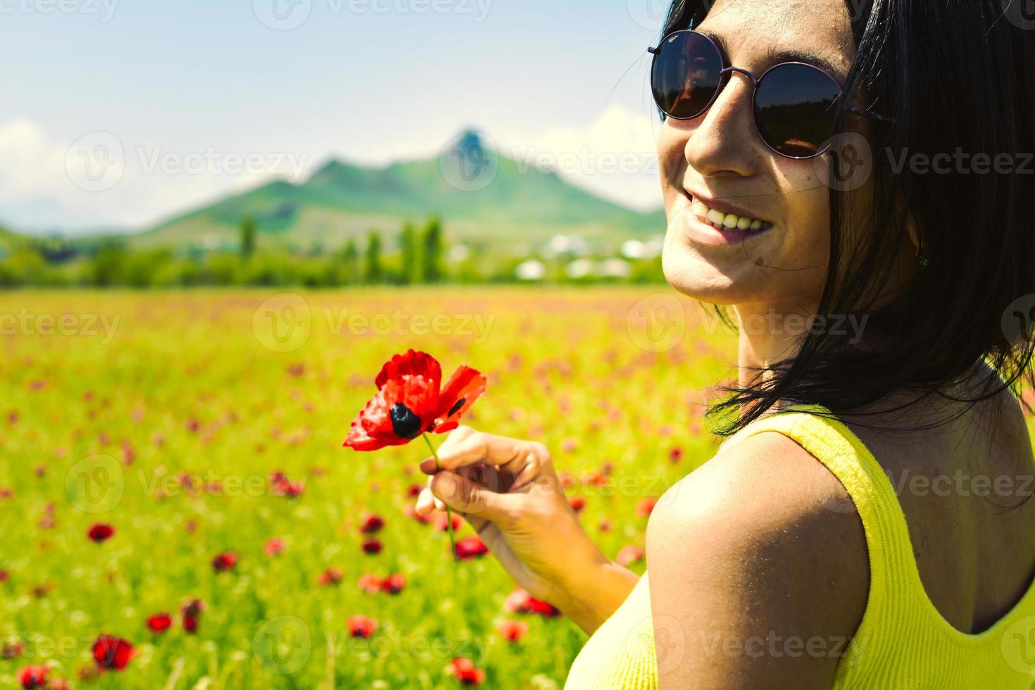 jonge, gelukkige blanke brunette vrouw met een enkele papaverbloem en geniet van een zonnige dag in het veld foto