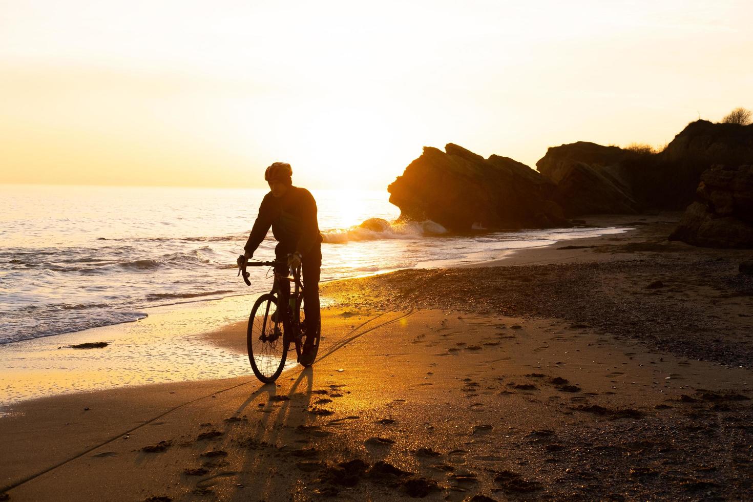 silhouet van jonge mannelijke fietser in helm op het strand tijdens prachtige zonsondergang foto