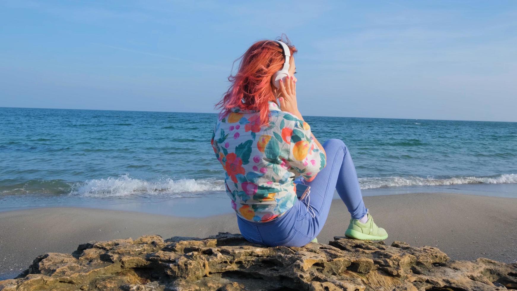 jonge vrouw met kleurrijk haar loopt op het zomerstrand en luistert naar muziek met een koptelefoon foto