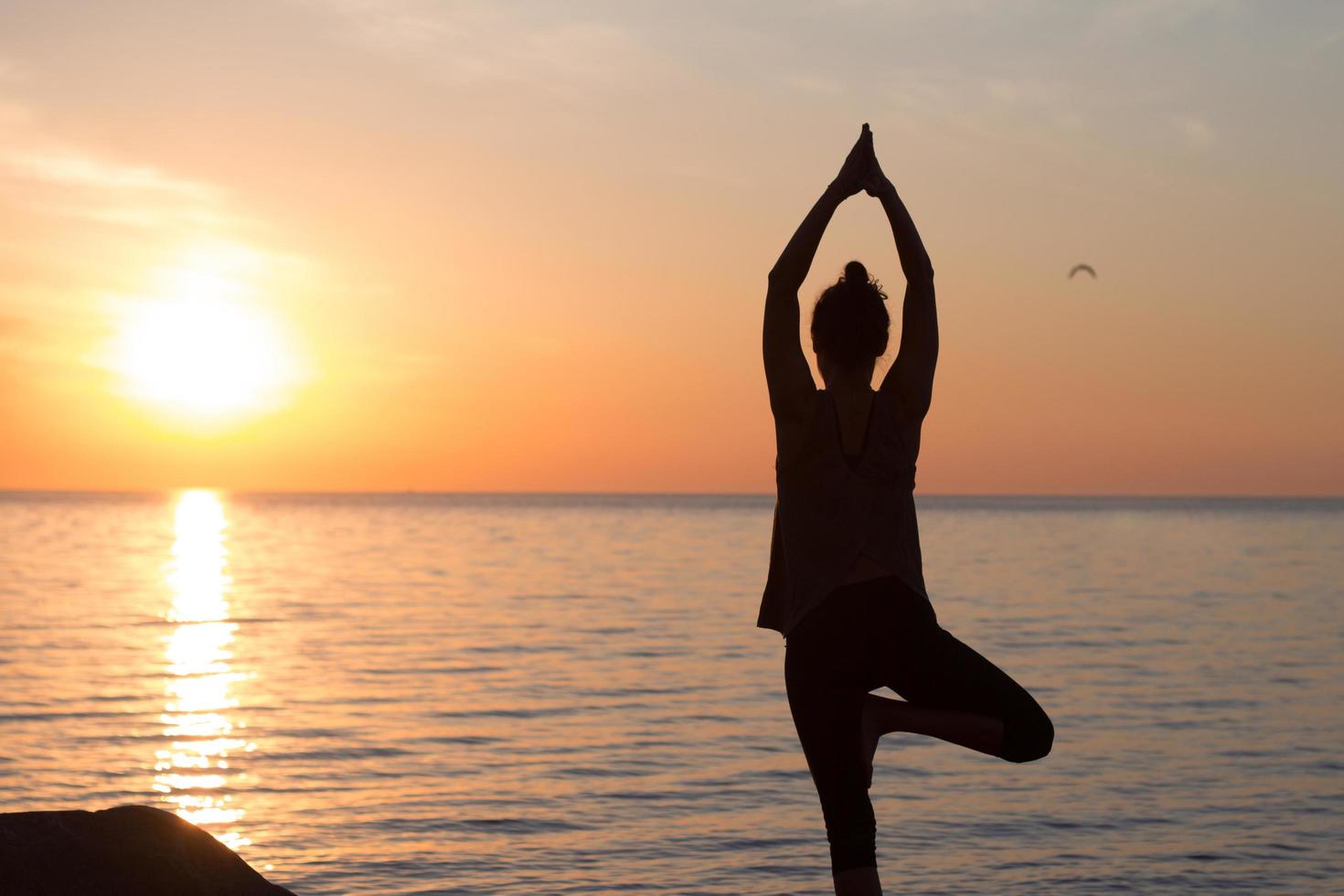 fitness gemengd ras aziatische vrouw in yoga pose op het ochtendstrand, mooie fit vrouw praktijk fitness exrxise stenen, ochtend zee of oceaan achtergrond foto