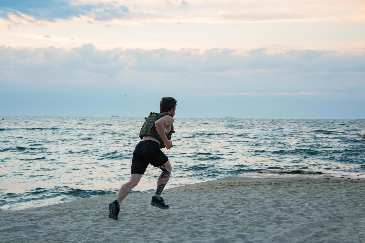 jonge, bebaarde atleet die buiten traint met gewogen vest, oefening met militaire plaatdrager foto