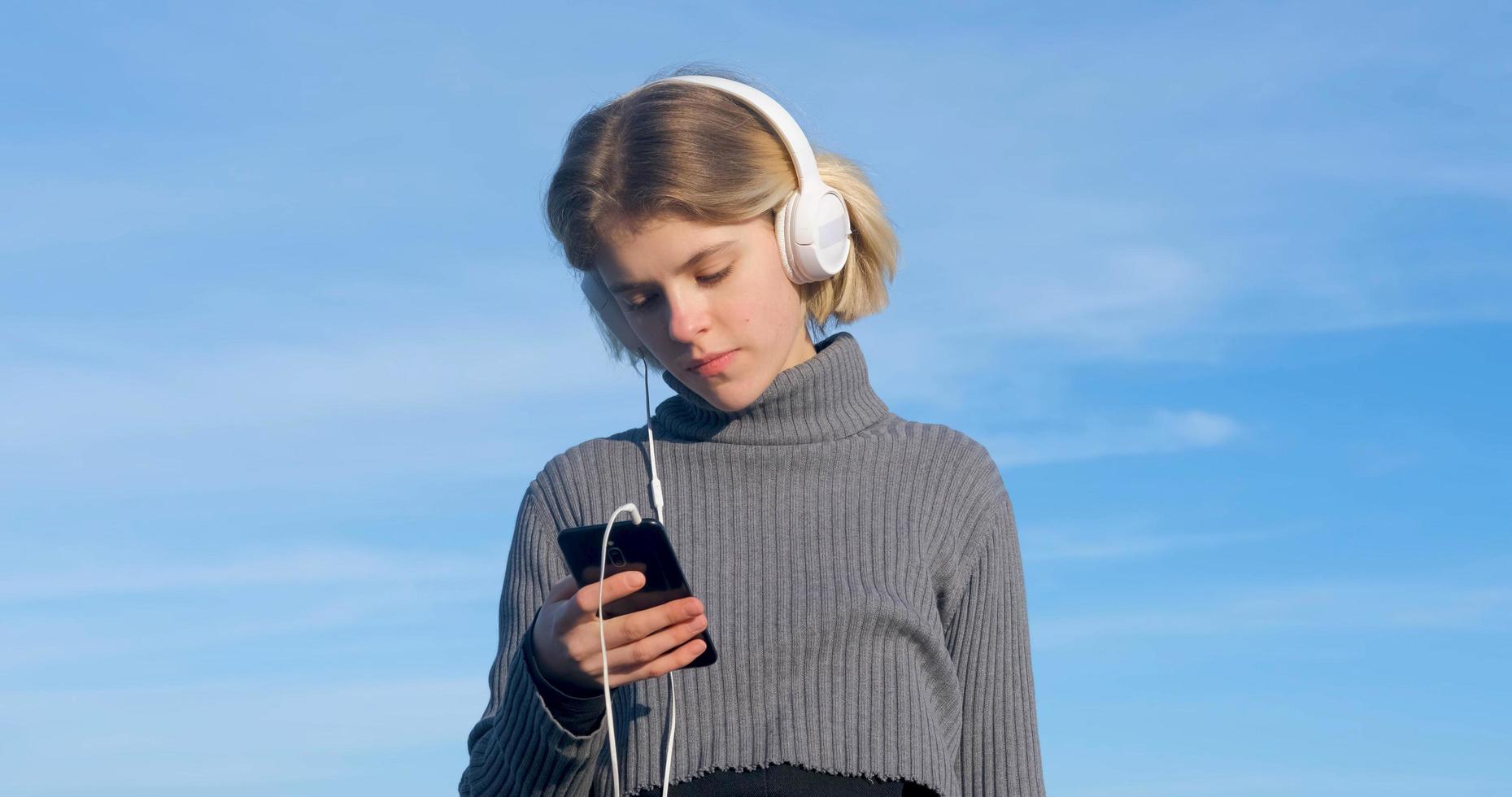 jonge knappe vrouw luistert naar muziek met een koptelefoon buiten op het strand tegen de zonnige blauwe hemel foto
