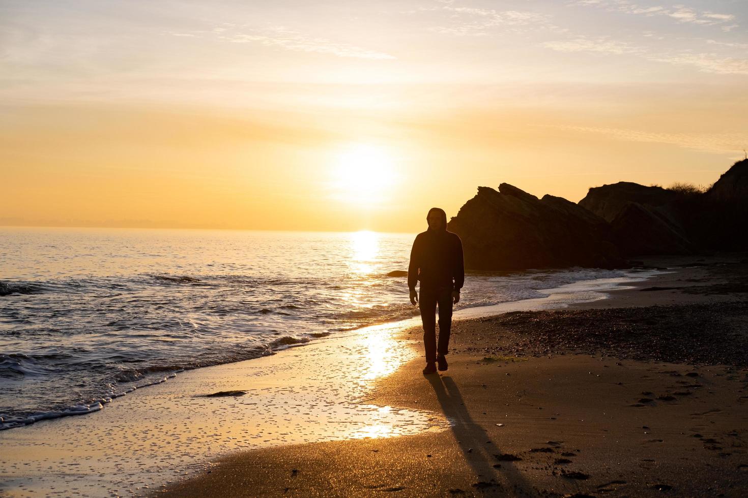 silhouet van mannelijke reiziger staat in de buurt van klif en kijkt naar de prachtige zonsondergang in de zee foto