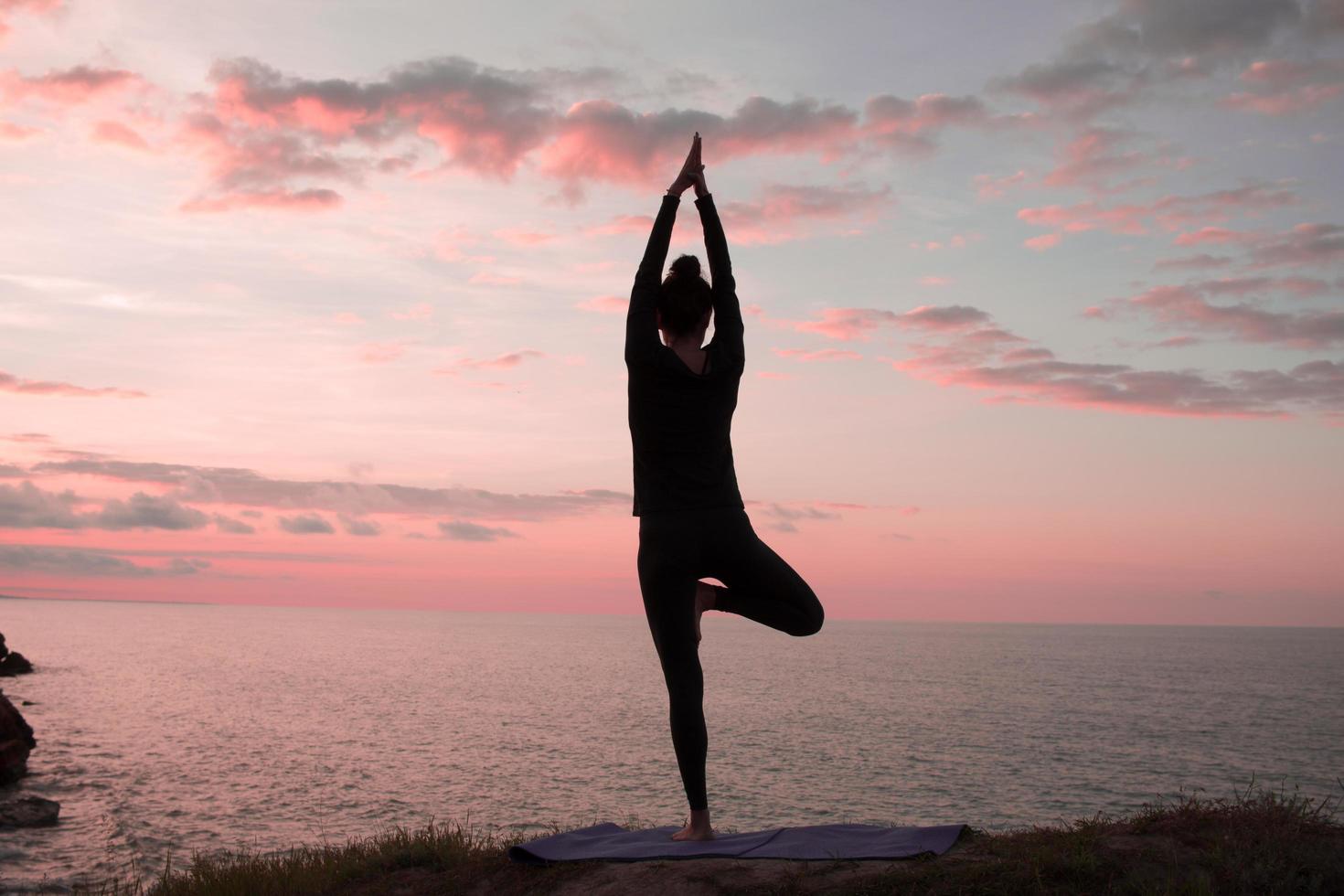 fit vrouw doet yoga stretching oefening buiten in prachtige bergen landschap. vrouw op de rots met zee en zonsopgang of zonsondergang achtergrond training asans. silhouet van vrouw in yogahoudingen foto