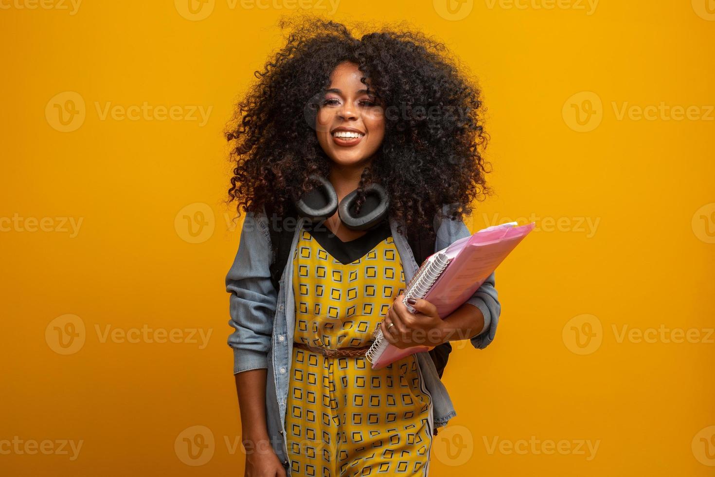 vrouwelijke student op de campus met boeken in haar armen. gele achtergrond. foto