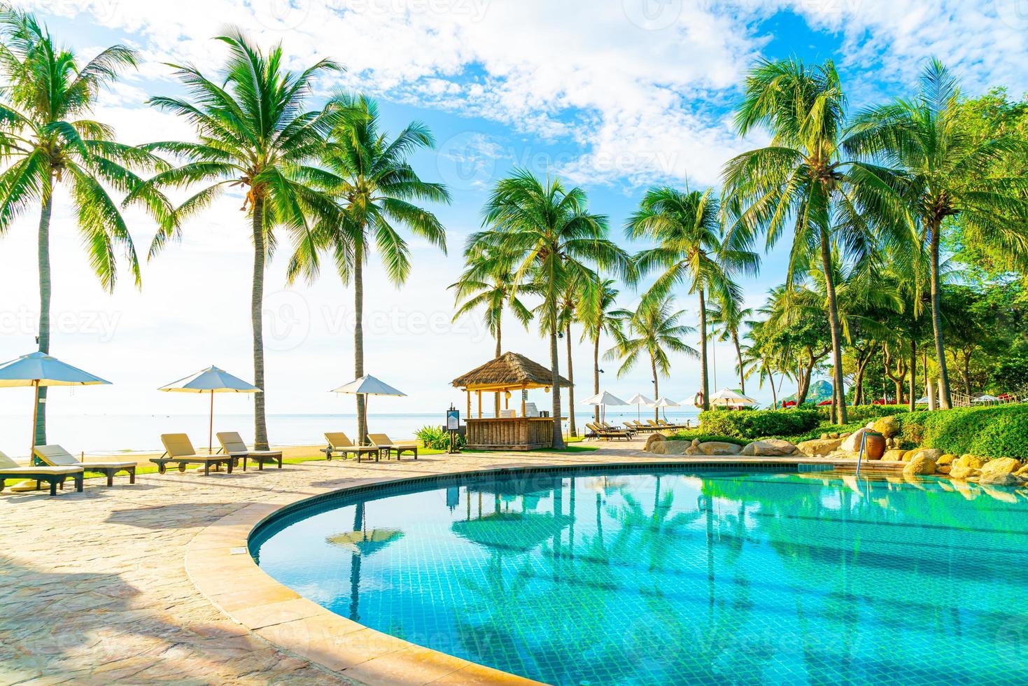 mooie luxe parasol en stoel rond buitenzwembad in hotel en resort met kokospalm op blauwe hemel foto