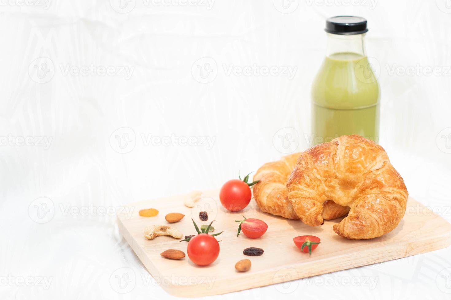 croissant met rode tomaten geïsoleerd op houten plaat, vers gebakken brood voor eenvoudig ontbijt. foto