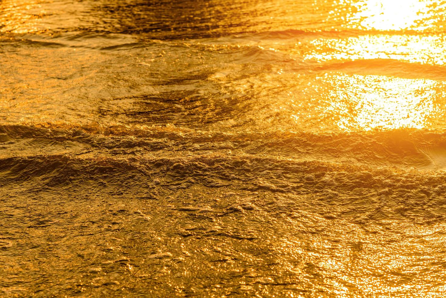 gouden licht weerkaatst op een watergolf in de zee en zand bij zonsondergang. puur gouden toon foto