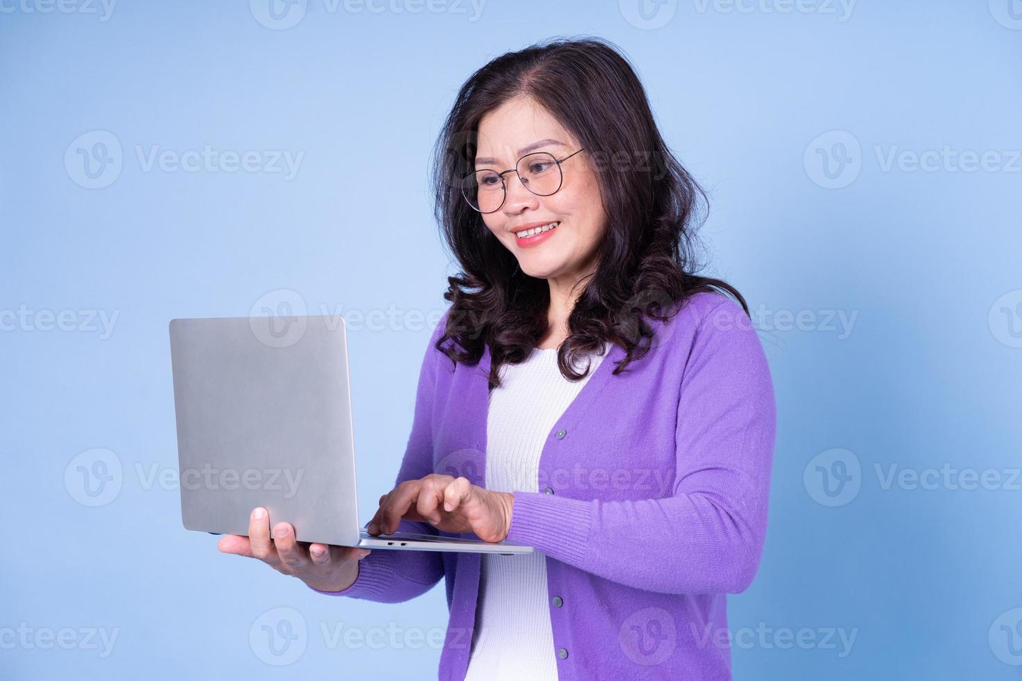 portret van een Aziatische vrouw van middelbare leeftijd die laptop op blauwe achtergrond gebruikt foto