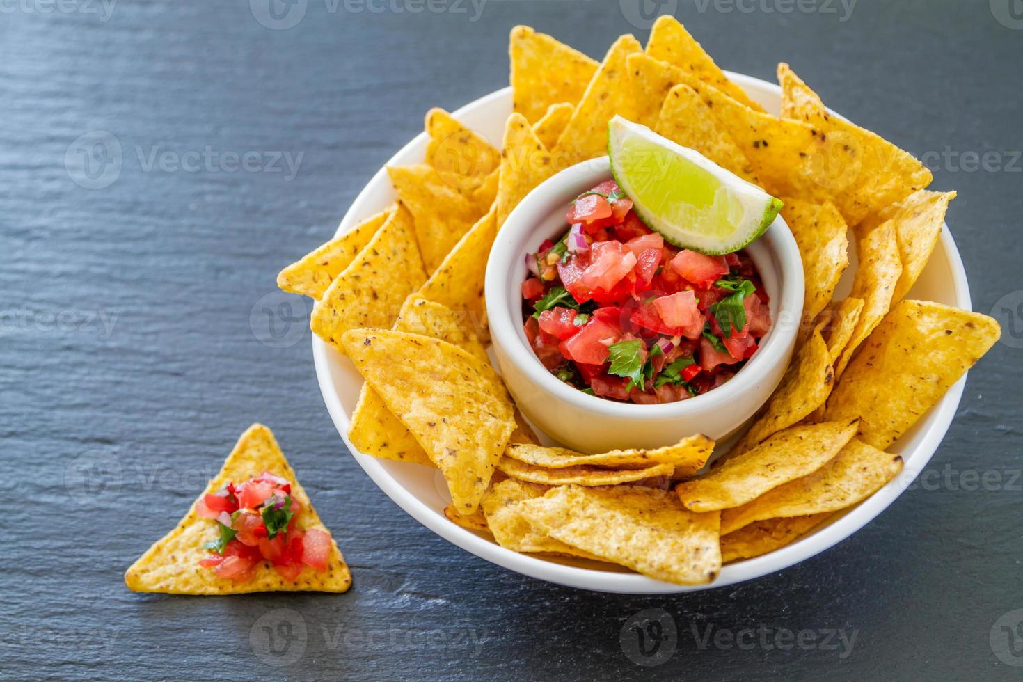 salsasaus en nacho's in witte kom, donkere steenachtergrond foto