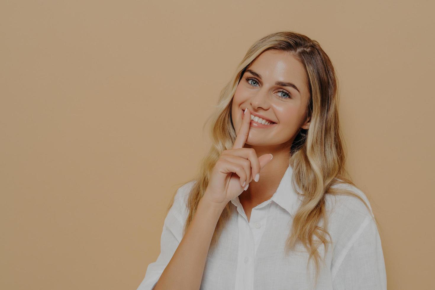 mooie jonge vrouw met lang blond geverfd haar toont een stil teken of houdt een gebaar stil foto