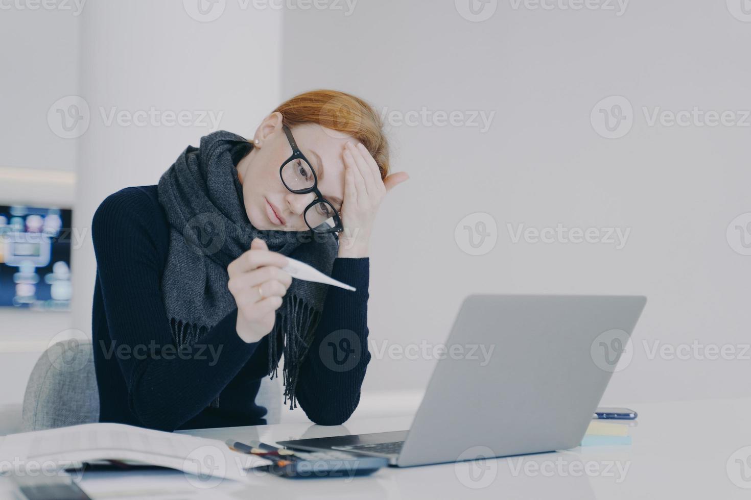 vermoeide executive werd verkouden en meet de temperatuur. trieste jonge blanke vrouw in sjaal is ziek. foto