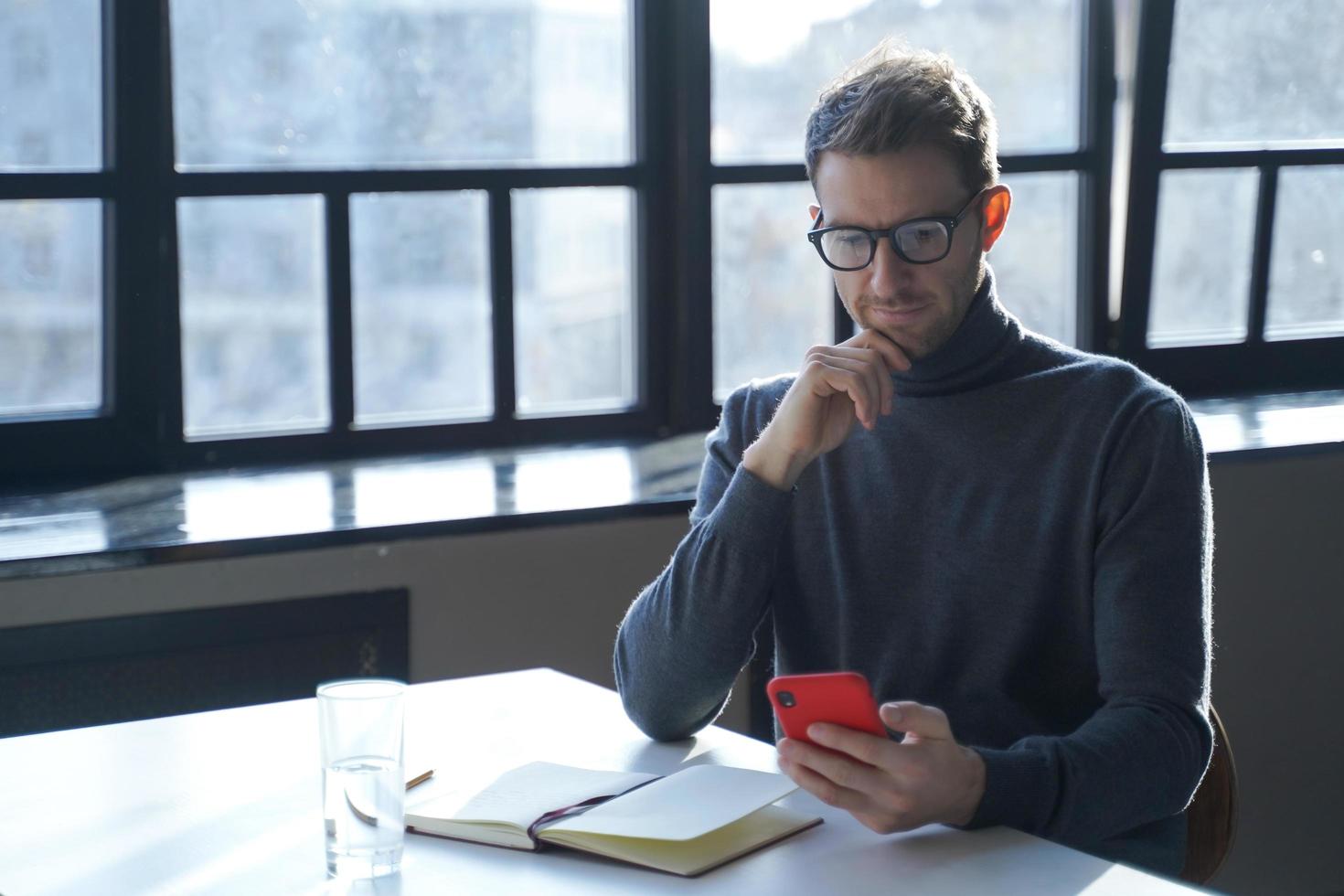 jonge Duitse zakenman die internetnieuws leest of e-mail controleert op smartphone terwijl hij aan het bureau zit foto