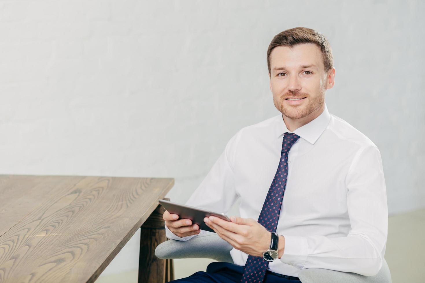 indoor shot van knappe mannelijke freelancer controleert melding op moderne tabletcomputer, verbonden met draadloos internet, deelt multimediabestanden met vrienden, kijkt direct naar de camera. communicatie foto