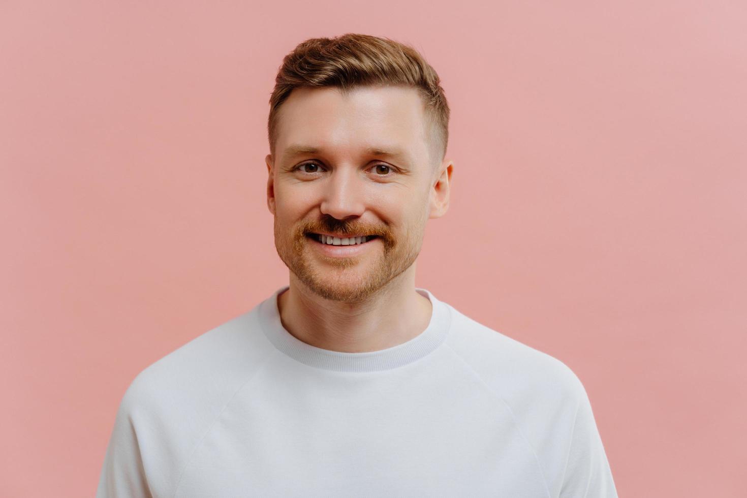 jonge positieve man die lacht op camera in roze studio achtergrond foto