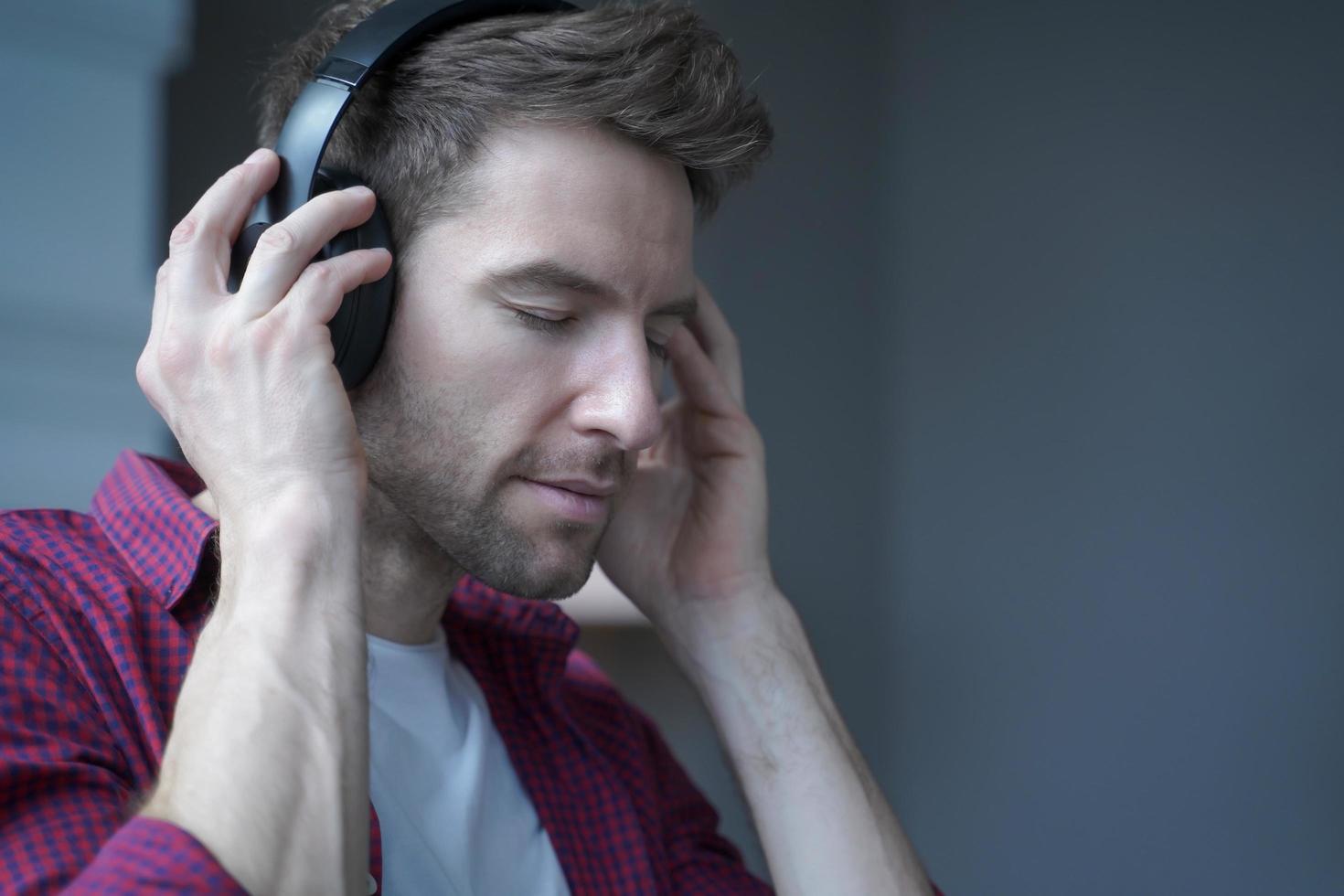 jonge tevreden Duitse man met gesloten ogen die thuis muziek luistert in een koptelefoon met een opgetogen gezicht foto