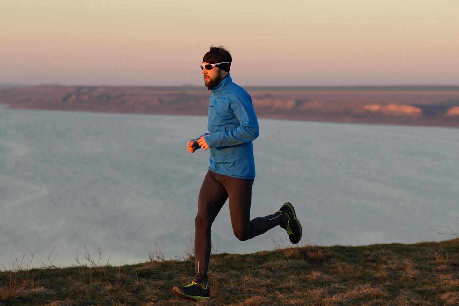 jonge man trailrunner training buiten in de velden, zonsondergang op de achtergrond van het meer foto