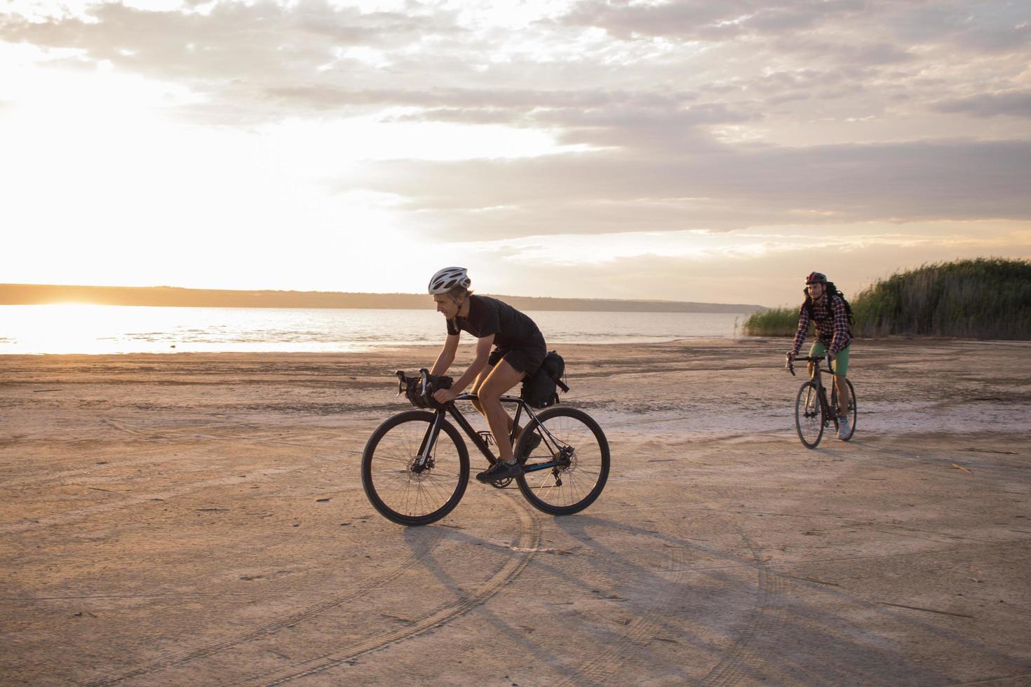 twee jonge mannen op een toerfiets met rugzakken en helmen in de woestijn op een fietstocht foto