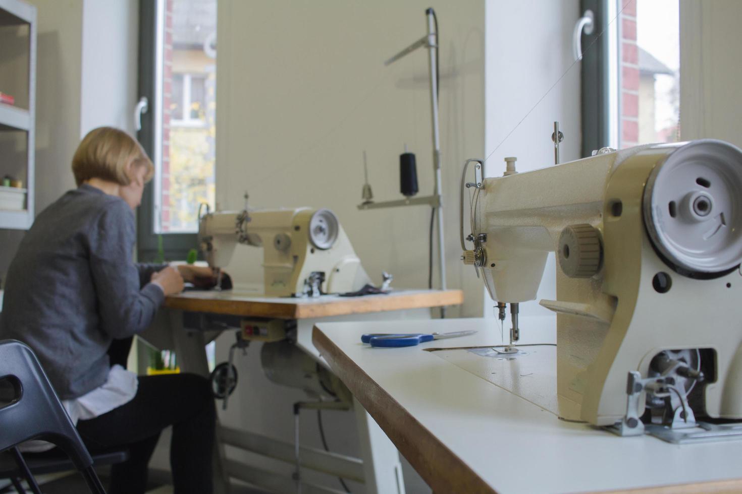 naaister aan het werk aan tafel, kleermaker vrouw werk in studio met kleding foto