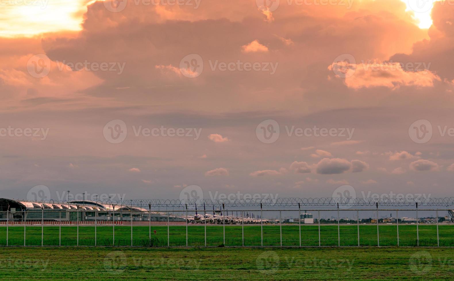 landschap van groen grasveld en hek van de luchthaven en prachtige avondrood. commercieel vliegtuig geparkeerd op het platform van de luchthaven. coronavirus had gevolgen voor de luchtvaartactiviteiten. hek voor veiligheid en beveiliging. foto