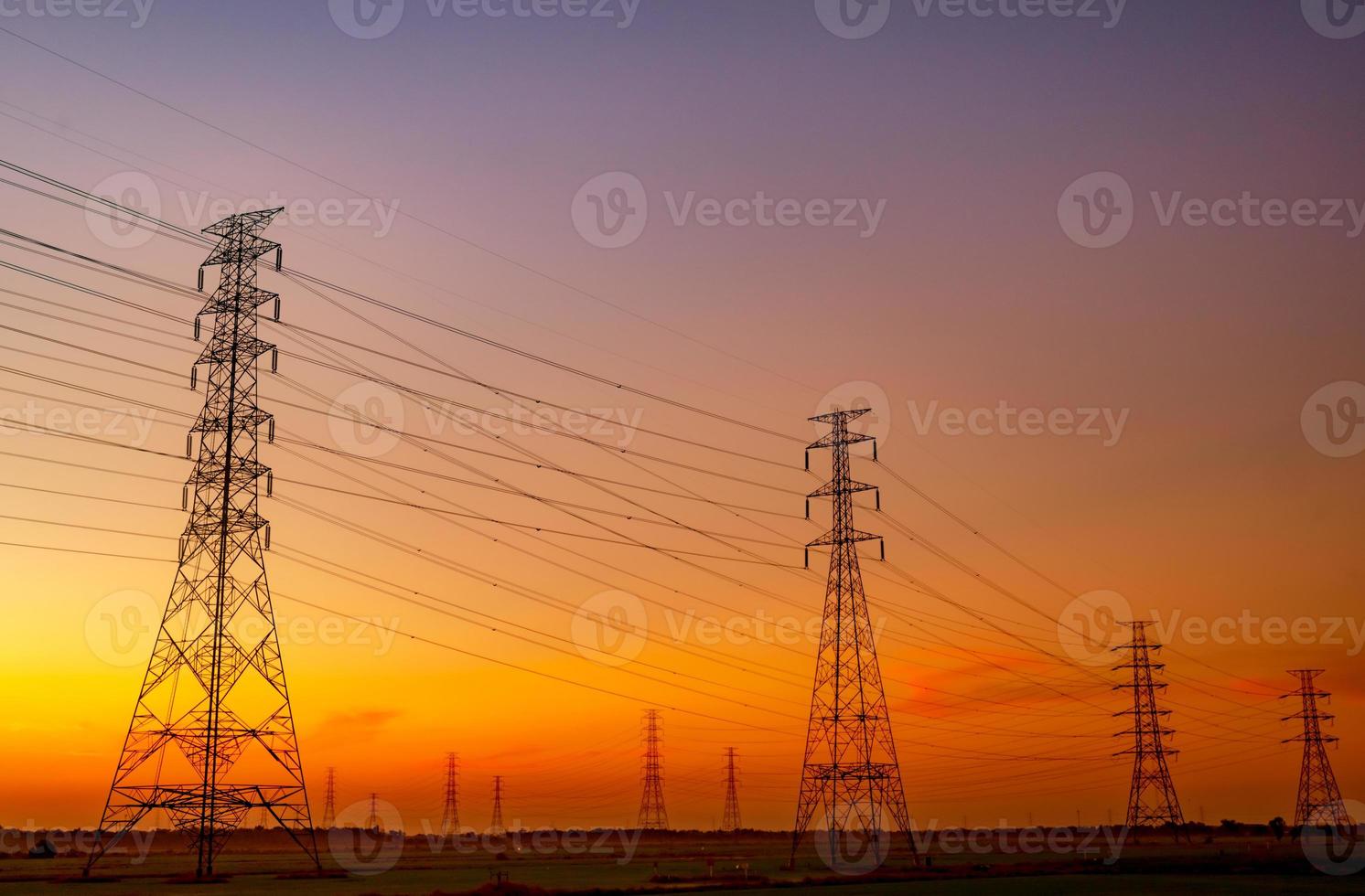 hoogspanning elektrische pyloon en elektrische draad met avondrood. elektriciteitspalen. macht en energieconcept. hoogspanningsnettoren met draadkabel op rijstveld in de buurt van industriële fabriek. foto