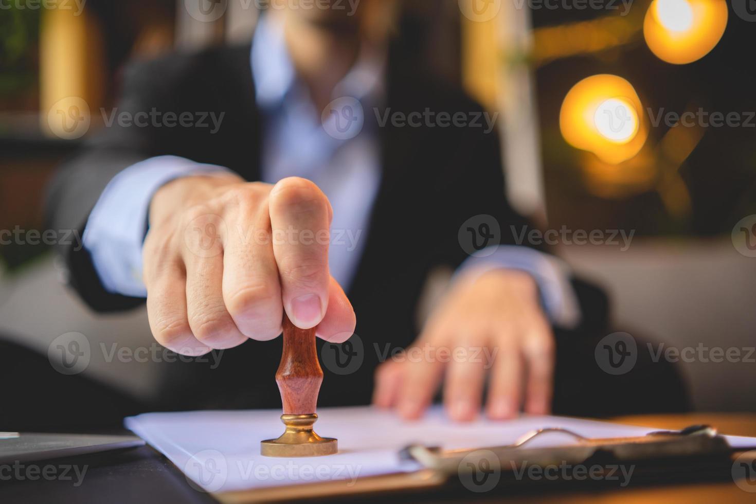 close-up van iemands hand stempelen met goedgekeurde stempel op goedkeuring certificaat document openbaar papier aan bureau, notaris of zakenmensen werken vanuit huis, geïsoleerd voor coronavirus covid-19 bescherming foto