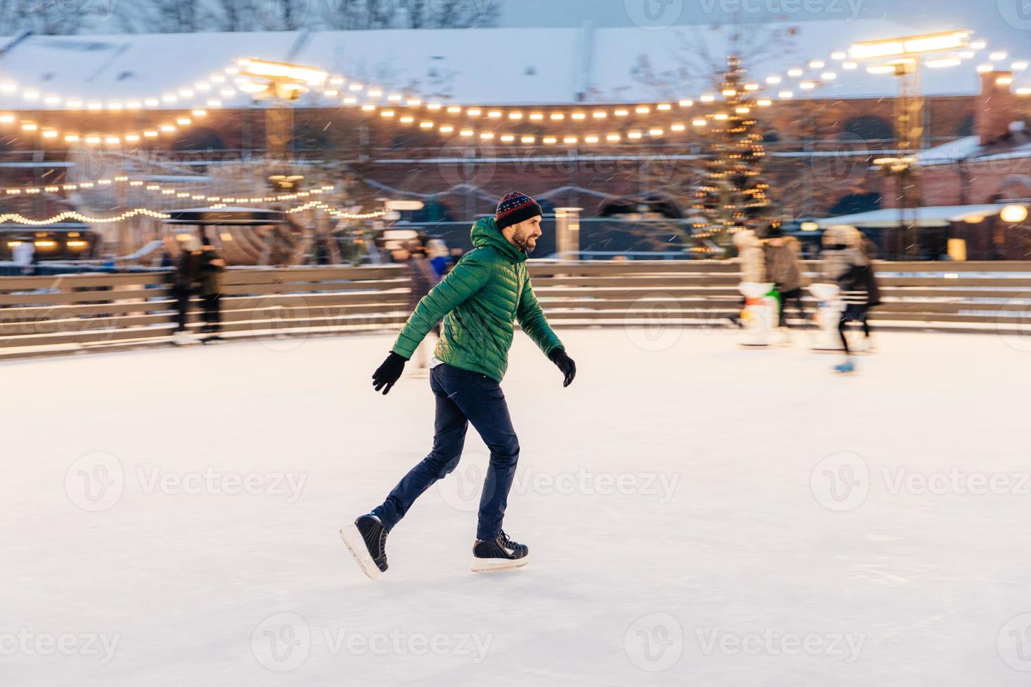 tevreden man in groene jas, draagt schaatsen, gaat schaatsen op ijs, brengt wintervakanties met gebruik door, toont zijn professionaliteit, geniet van sneeuwweer. winter leuke buitenactiviteiten foto