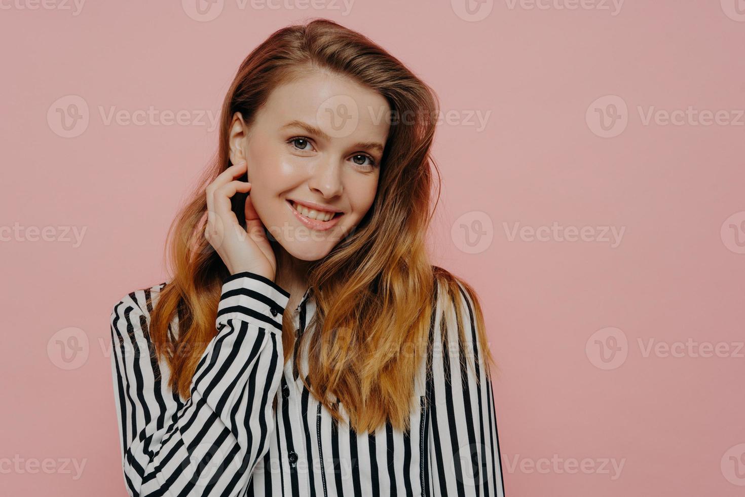 positieve jonge vrouw die lacht op camera poseren tegen roze muur foto