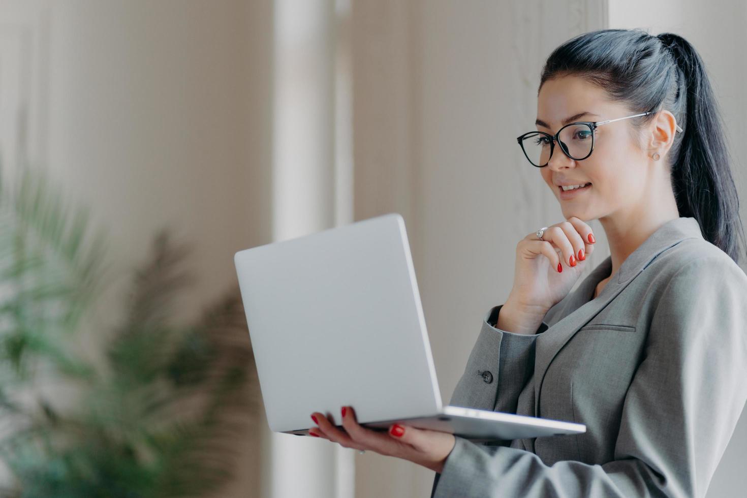 foto van mooie brunette vrouw houdt kin vast, geconcentreerd in laptopscherm, bestudeert financiële markt, gericht op externe baan, bereidt publicatie voor. freelacer bekijkt webinar om vaardigheden te verbeteren