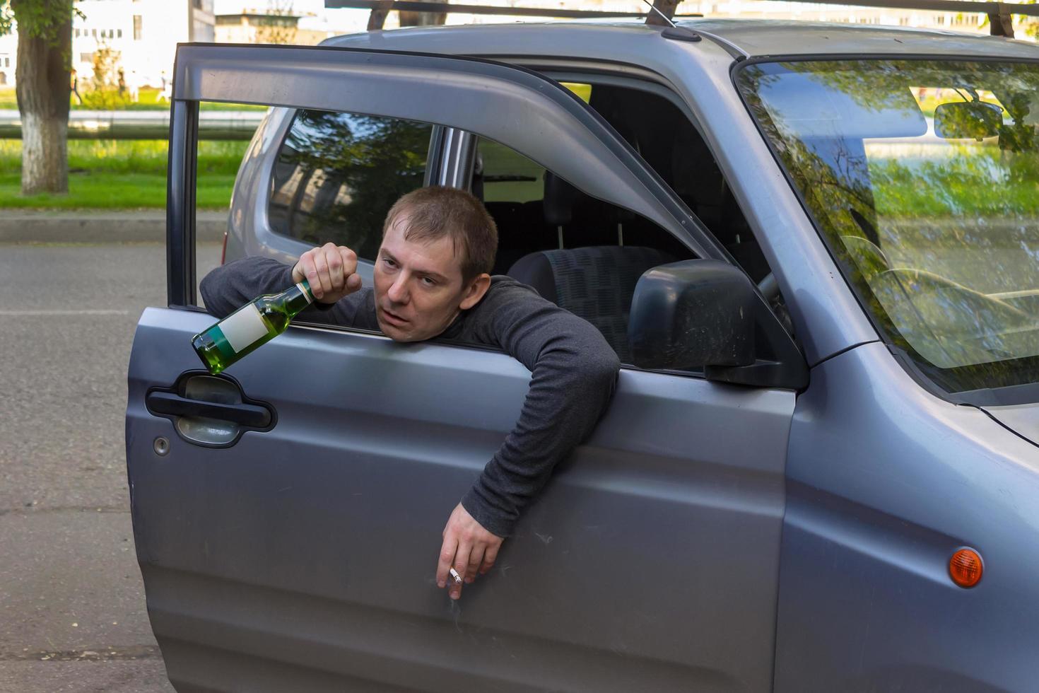 dronken automobilist hangt aan de deur met een flesje bier foto