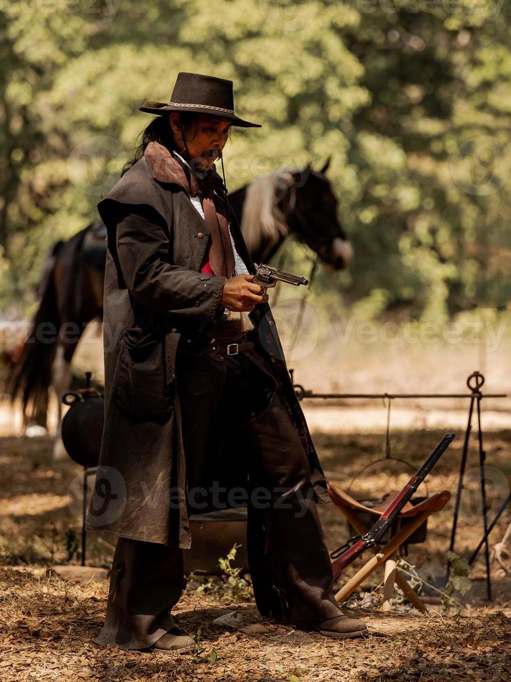 een senior cowboy die met een pistool staat om de veiligheid van het kamp in het westelijke gebied te bewaken foto