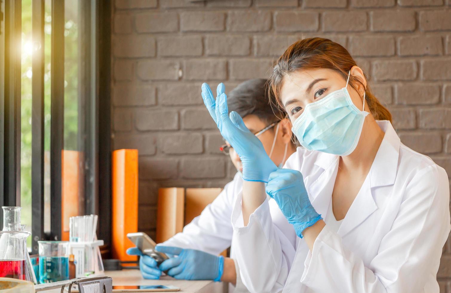 Wetenschappersteam dat onderzoek doet in een klinisch laboratorium, jonge vrouw met een medisch masker en een medisch bosje dat naar de camera kijkt foto