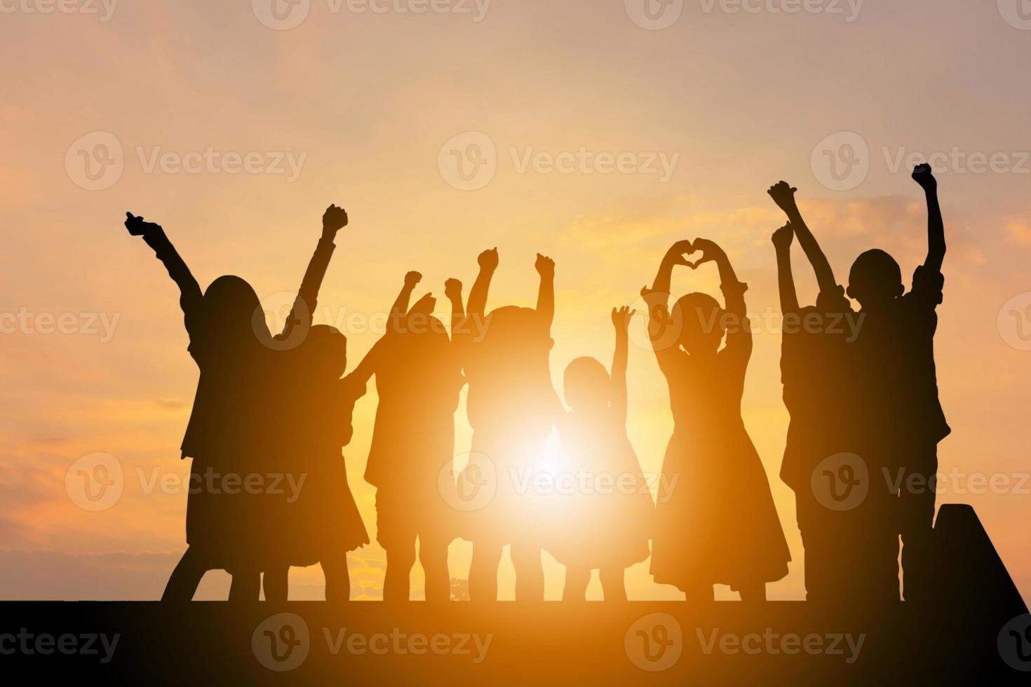 silhouet van gelukkige kinderen groep met uitknippad spelen met zonsondergang achtergrond foto