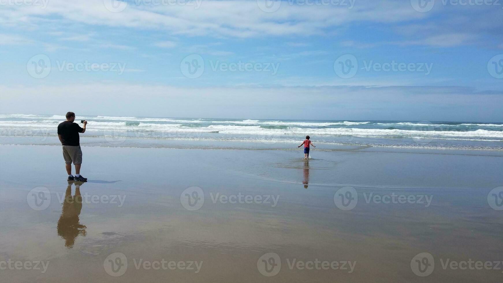 vader neemt foto van zoon in zand en water op het strand