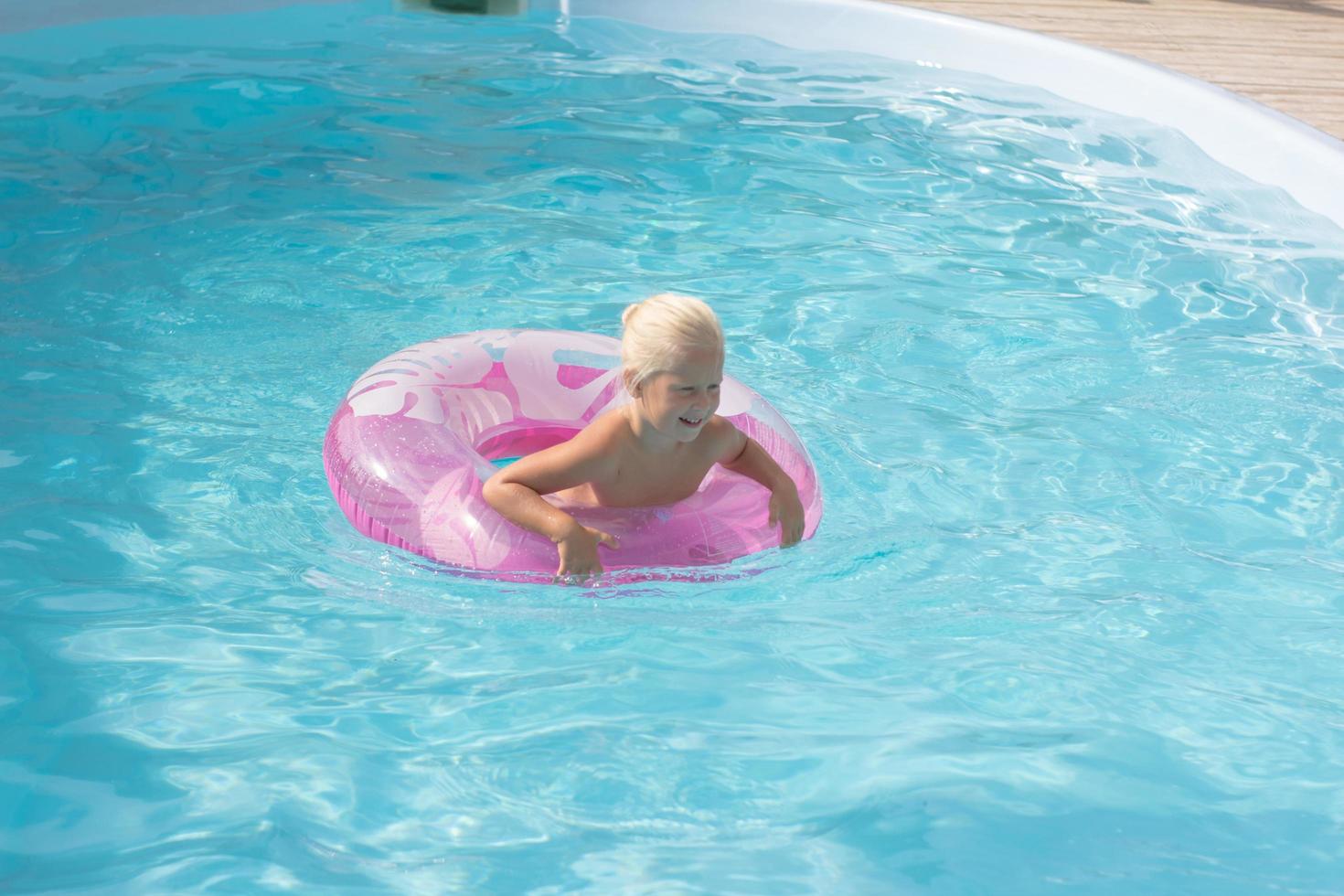 blonde jongen heeft plezier in het zwembad, kleine meid zwemt in de zomer foto