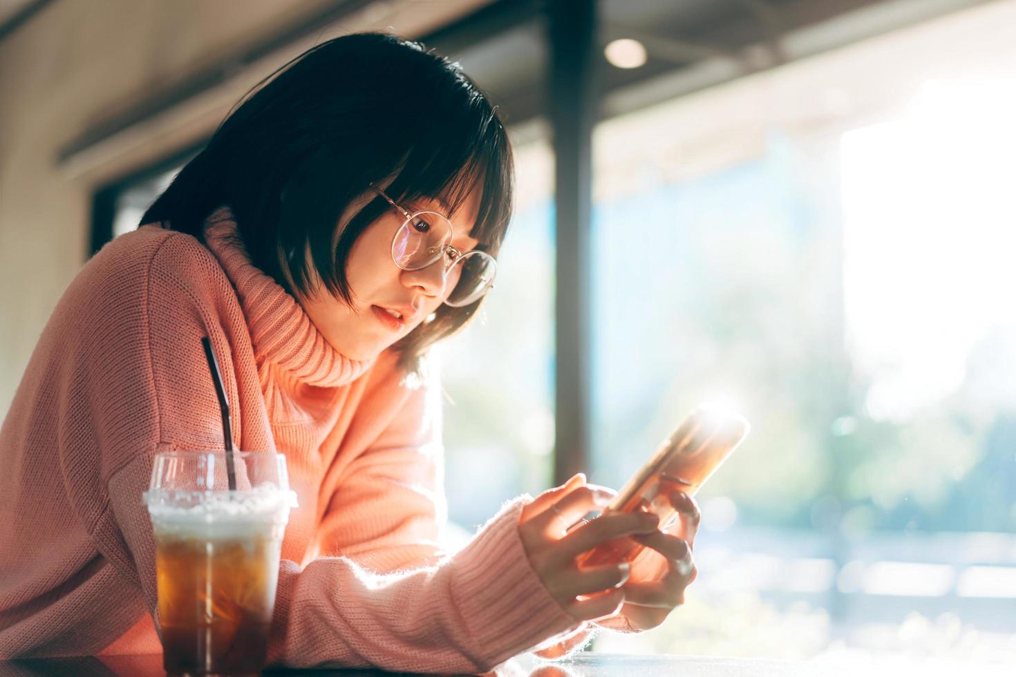 jonge volwassen aziatische vrouw die mobiele telefoon gebruikt voor sociale media-achtergrond met raam en warm zonlicht in de winter foto