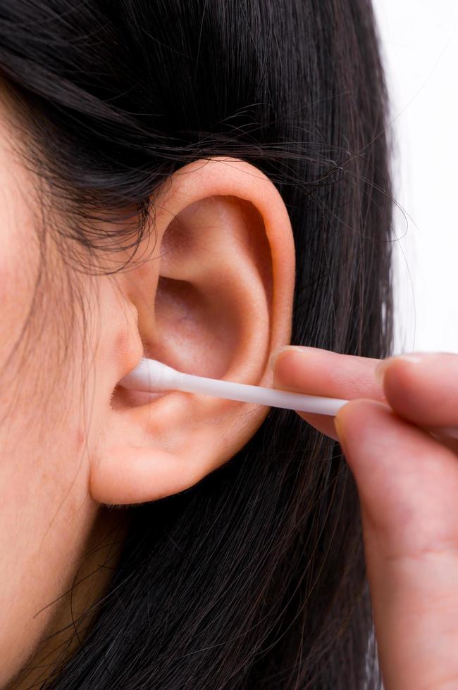 vrouw met zwarte haren maakt haar oren schoon met een wit wattenstaafje. persoonlijk hygiëneconcept. foto