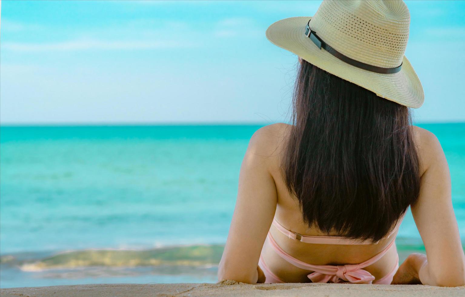 achteraanzicht van gelukkige jonge Aziatische vrouw in roze zwembroek en strohoed ontspannen en genieten van vakantie op tropisch paradijs strand bij zonsondergang. meisje in zomervakantie mode. schoonheid sexy model. zomerse sferen. foto